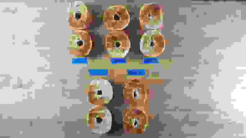 10 bagel halves with varying browning laid out on a countertop with distinguishing labels from respective toaster brands.