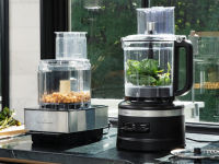 Cuisinart and KitchenAid food processors filled with ingredients and placed on a countertop in front of a window