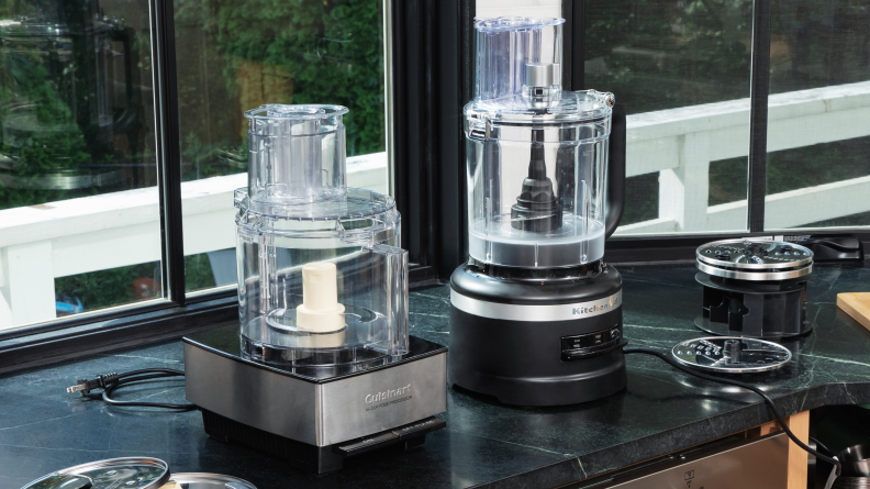 The Cuisinart and KitchenAid food processors sit on a counter with their slicing disks on either side.